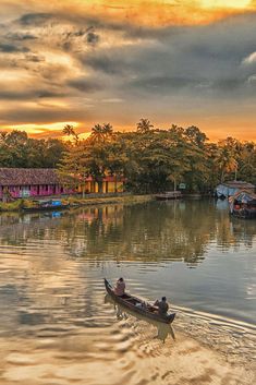 two people in a small boat on the water at sunset or dawn with colorful houses and trees behind them