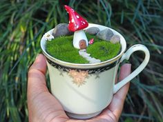 a hand holding a coffee cup filled with grass and mushrooms