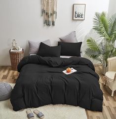 a bed with black sheets and pillows in a room next to a potted plant