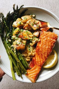 a white plate topped with fish, asparagus and lemon wedges next to a fork