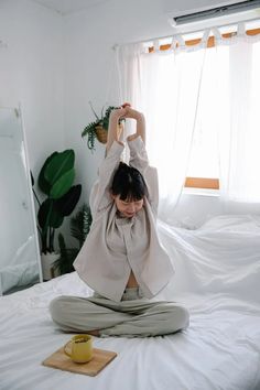 a woman is doing yoga on her bed in front of a mirror and coffee mug