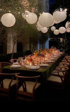 a long table with paper lanterns hanging from it's ceiling and place settings on the tables