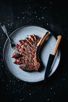 a piece of steak on a plate with a knife and fork next to it, against a black background