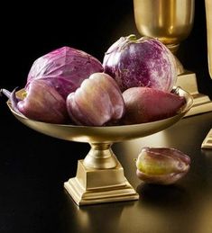 a bowl filled with red onions next to two golden vases on a black table