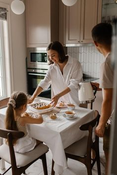 a woman and two children sitting at a kitchen table with food in front of them