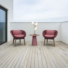 two red chairs sitting on top of a wooden floor next to a table with a lamp