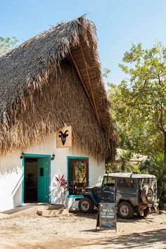 an old jeep parked in front of a thatched roof house with a sign on the door