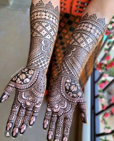 two hands with henna tattoos on them, one is showing the intricate pattern and the other