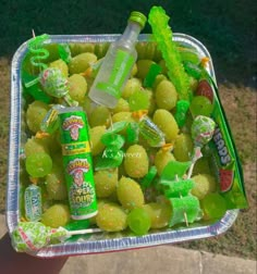 a plastic container filled with green fruit next to a can of soda on top of a sidewalk