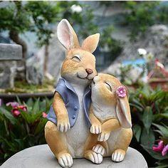 a statue of two rabbits sitting on top of each other in front of some flowers