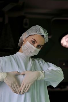 a woman in white gown and surgical mask standing with her hands on her hips, looking at the camera