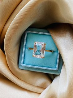 an engagement ring is sitting on top of a blue velvet box in the middle of a beige fabric