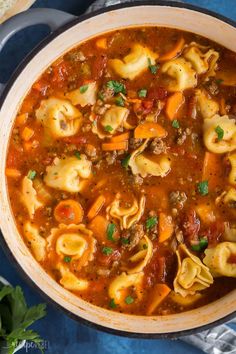 a pot filled with tortellini soup on top of a blue tablecloth next to a spoon