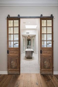 an open door leading to a bathroom with a tub in the middle and wooden floors