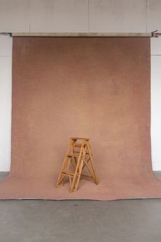 a small wooden chair sitting on top of a pink floor next to a white wall