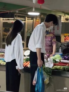 two people standing in front of a counter filled with vegetables