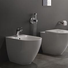 two white toilets sitting next to each other on a tiled floor in front of a gray wall