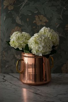 two white flowers in a copper vase on a marble table