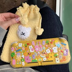 a person holding a yellow cell phone case with animal stickers on it and a crocheted bag next to it