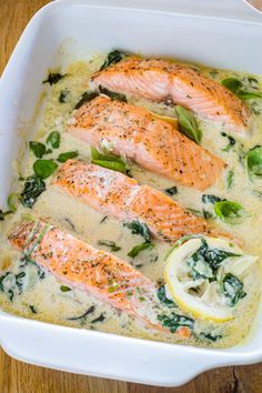 baked salmon with spinach and lemon in a white casserole dish on a wooden table