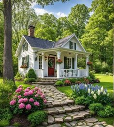 a small white house surrounded by lush green trees and flowers in the front yard with steps leading up to it