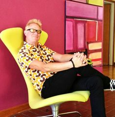 a man sitting on top of a yellow chair in front of a pink and purple wall