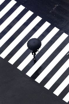 an overhead view of a person walking across a crosswalk in the rain with an umbrella