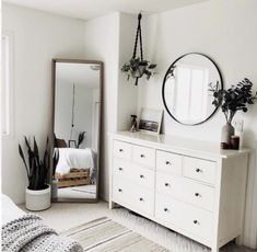 a bedroom with white furniture and plants on the dresser next to a large round mirror