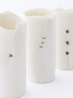 three white vases with black beaded details on the handles and sides, all lined up against one another