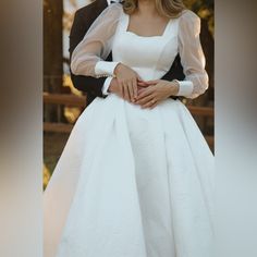 a bride and groom pose for a wedding photo in front of a wooden fence with their arms around each other