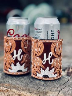 two beer cans sitting on top of a piece of wood next to each other,