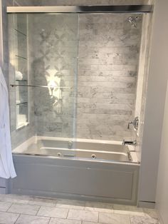 a bathroom with a glass shower door and white tile flooring, along with a walk in tub