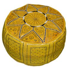 a yellow and black round ottoman with decorative designs on the top, sitting in front of a white background