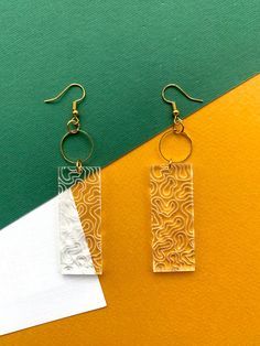 two pairs of earrings sitting next to each other on top of a green and yellow surface