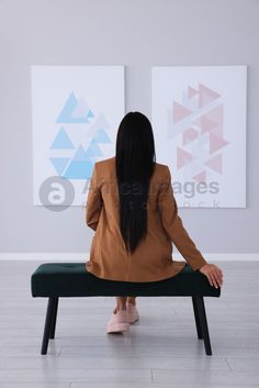 a woman sitting on top of a bench in front of two large paintings behind her