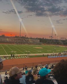 the sun is setting over a football field as people sit at tables in front of them