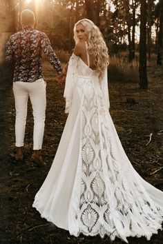 a bride and groom walking through the woods holding hands with each other in their wedding gowns