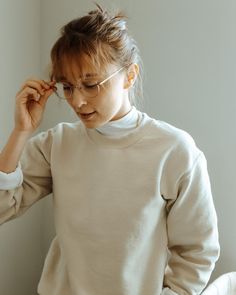 a woman in a white sweater is holding her glasses up to her eyeglasses