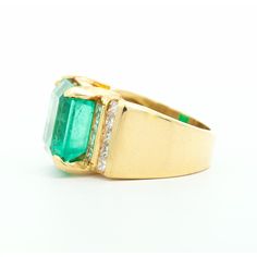 a gold ring with an emerald and diamond set in the center, on a white background