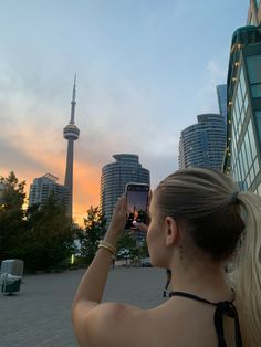 a woman is taking a photo with her cell phone in front of the cn tower