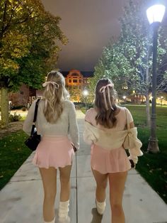 two girls walking down a sidewalk at night with their back to the camera, both wearing short skirts and knee high socks