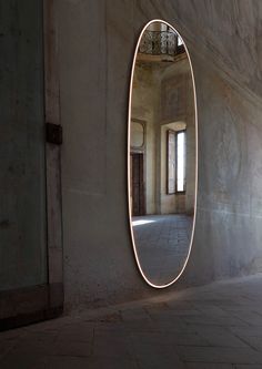 an oval shaped mirror in the middle of a room with concrete walls and flooring