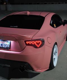 a pink car parked in a parking lot with its tail lights turned on at night