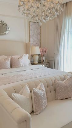 a large white bed sitting in a bedroom next to a chandelier and window