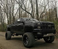 the black truck is parked on the side of the road in front of some trees