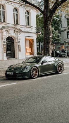 a dark green sports car parked on the side of the road next to a tree