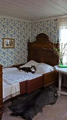 a black and white cat laying on top of a bed in a room with floral wallpaper