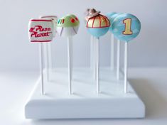 three cake pops with different designs on them sitting on a white stand in front of a white wall