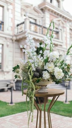 a vase with white flowers sitting on top of a table next to a bench in front of a building