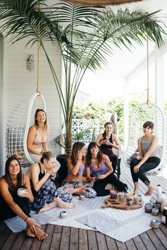 a group of women sitting on top of a wooden floor next to each other in front of a palm tree